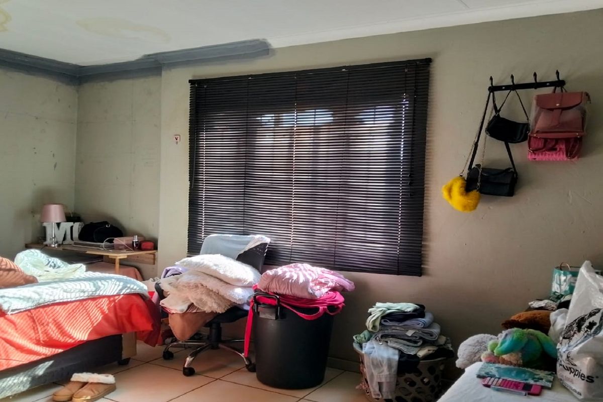 A bedroom featuring tiled flooring and venetian blinds, currently showing signs of ceiling water damage and wall surface wear.