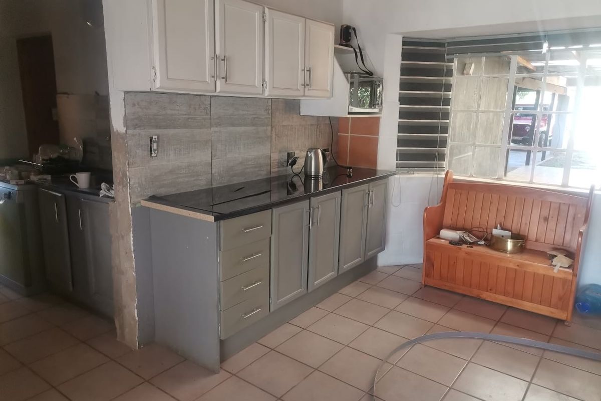 A functional kitchen area featuring built-in cabinetry, dark countertops, and tiled flooring, with an adjacent scullery area visible.