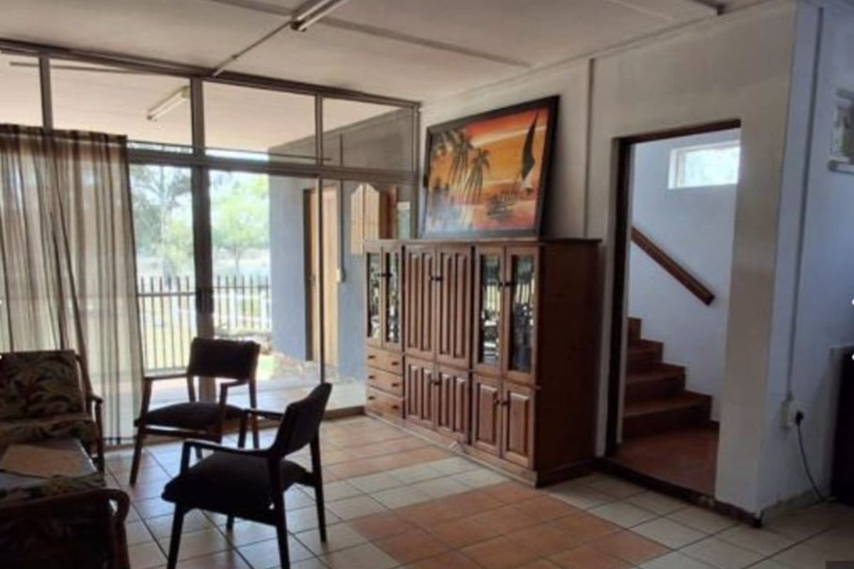 A sunlit living area featuring large glass sliding doors, tiled flooring, and an adjacent staircase leading to the upper level.