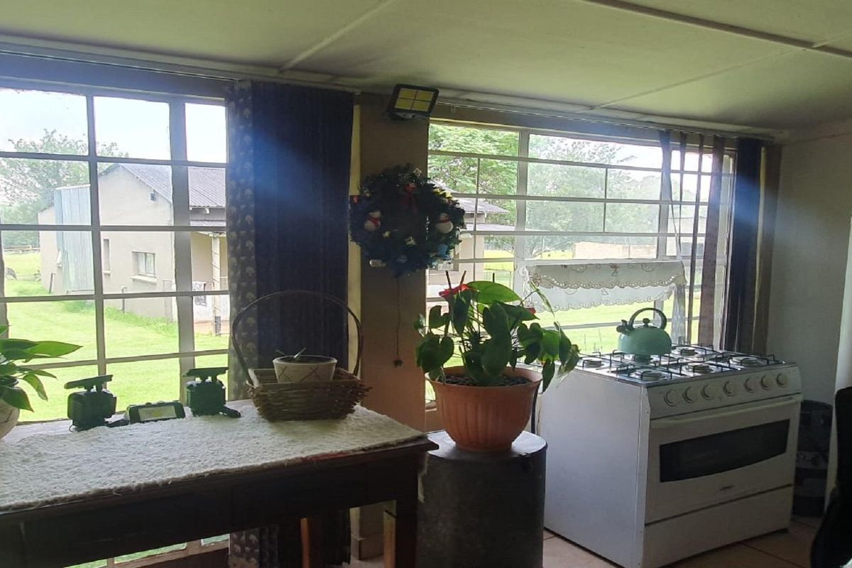 A functional kitchen area featuring large windows with security bars, a freestanding gas stove, and tiled flooring, overlooking the farm grounds.