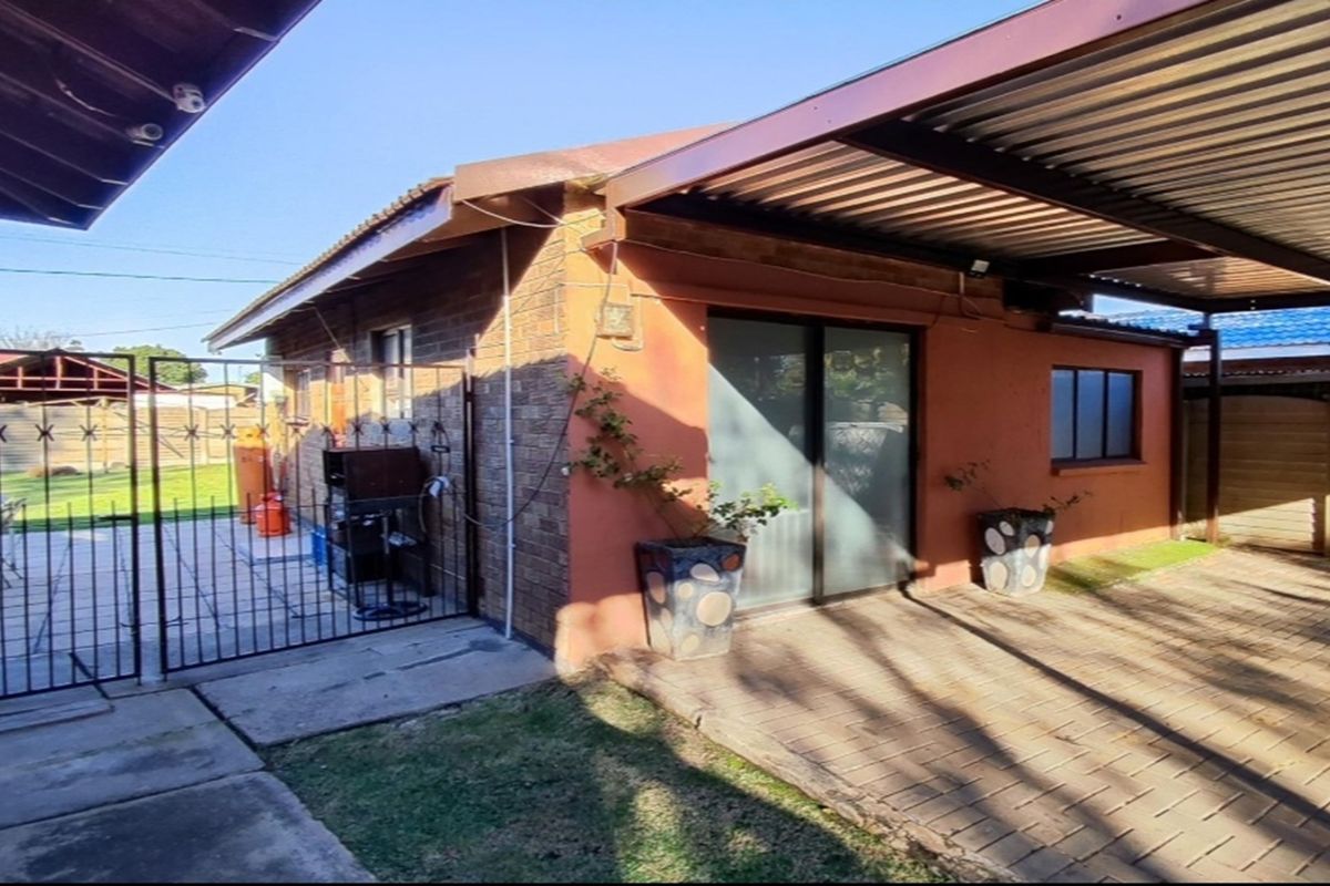 Exterior view of the property featuring a paved driveway, covered carport area, and a side gate leading to a rear patio space.