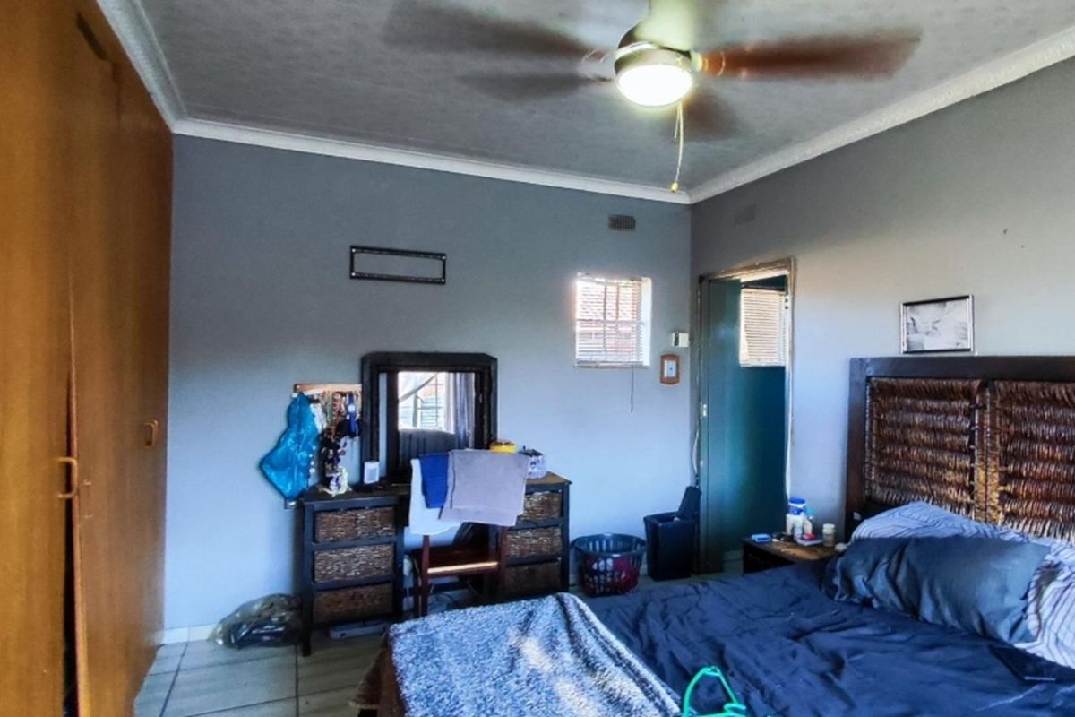 A functional bedroom featuring built-in wooden cupboards, a ceiling fan, and tiled flooring, offering a practical layout for comfortable living.
