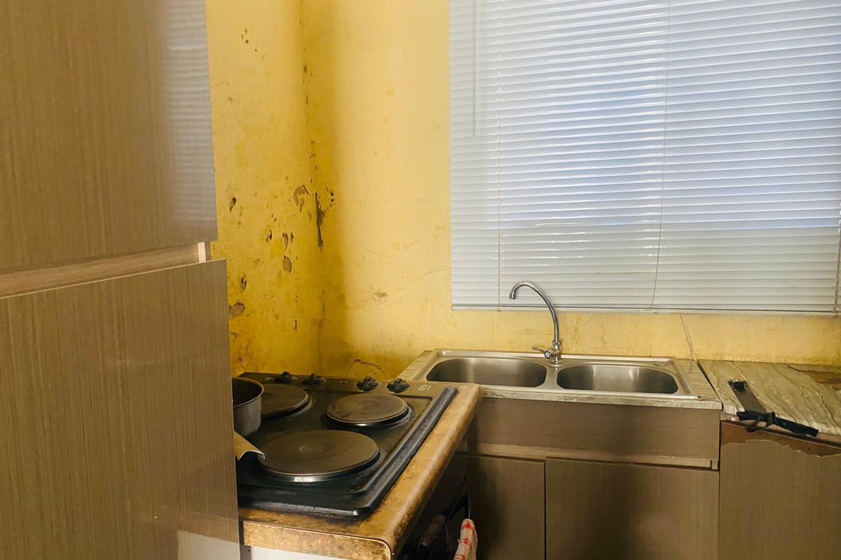 A dated kitchen area featuring a built-in electric hob, double basin sink, and cabinetry, requiring significant cosmetic renovation and wall repairs.