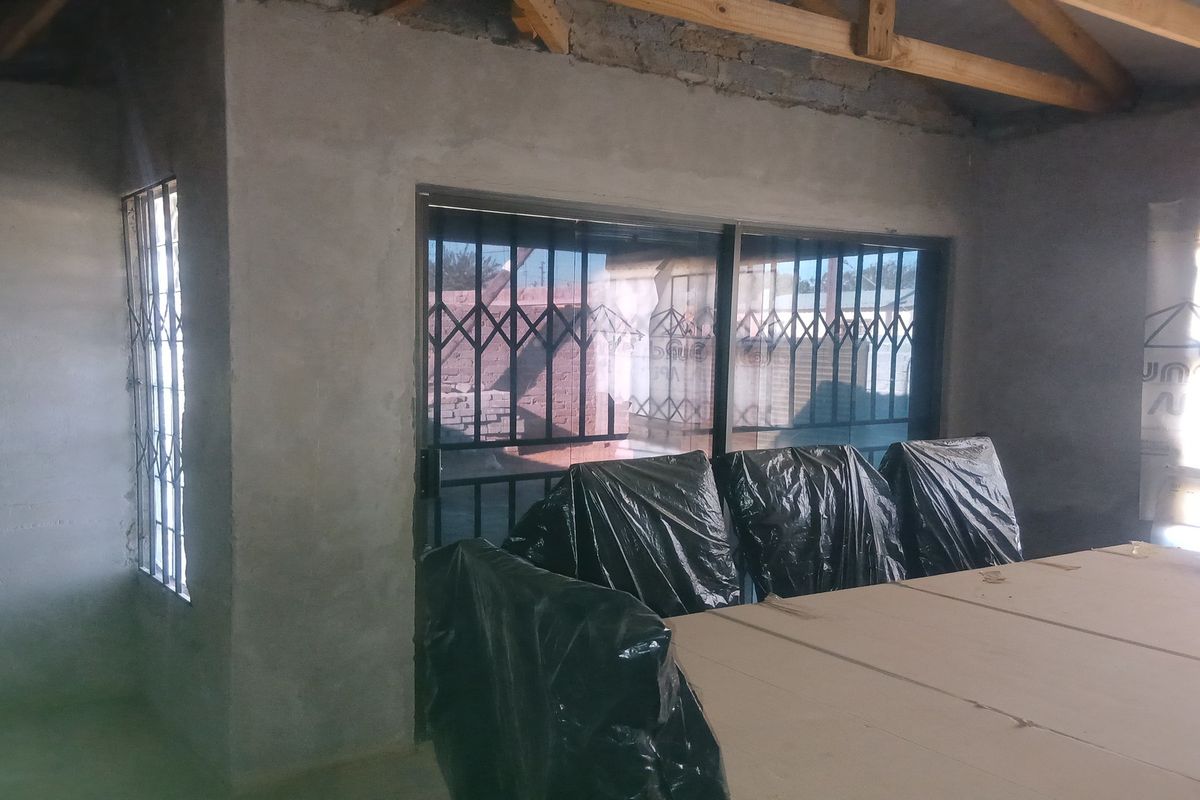 An unfinished interior space featuring exposed roof trusses, raw cement walls, and sliding glass doors with security gates.