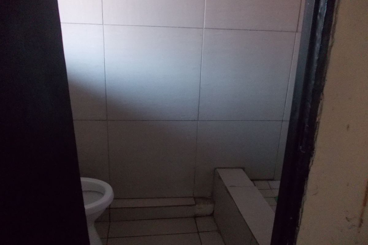 A small, functional bathroom featuring tiled walls and flooring, including a toilet and a raised tiled platform.