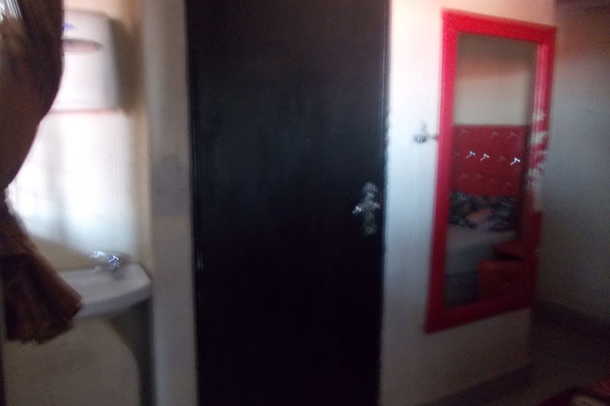 A small interior space featuring a wall-mounted basin, a dark internal door, and a red-framed mirror.