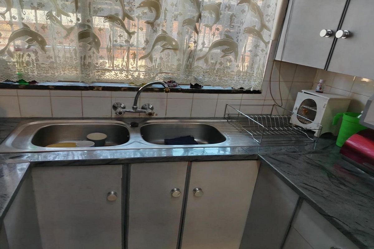 A functional kitchen area featuring a double bowl stainless steel sink, laminate countertops, and built-in cabinetry with a tiled backsplash.