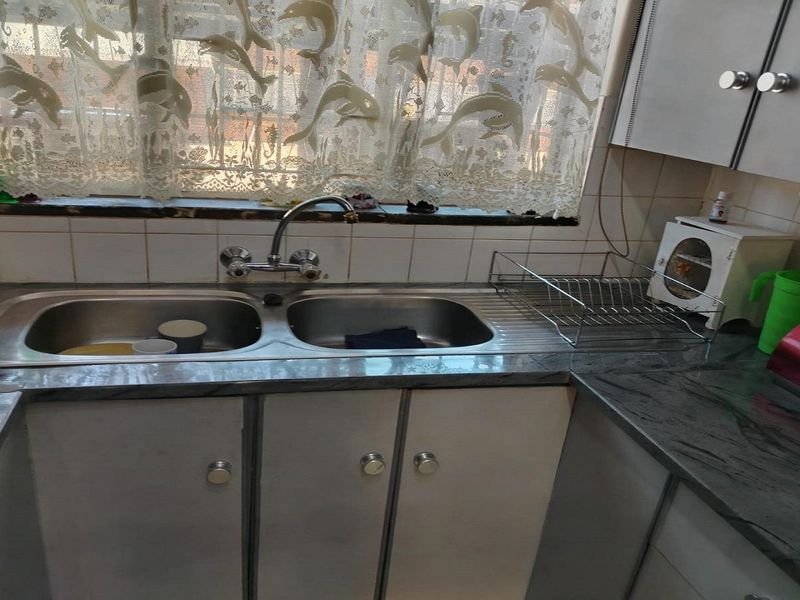 A functional kitchen area featuring a double bowl stainless steel sink, laminate countertops, and built-in cabinetry with a tiled backsplash.