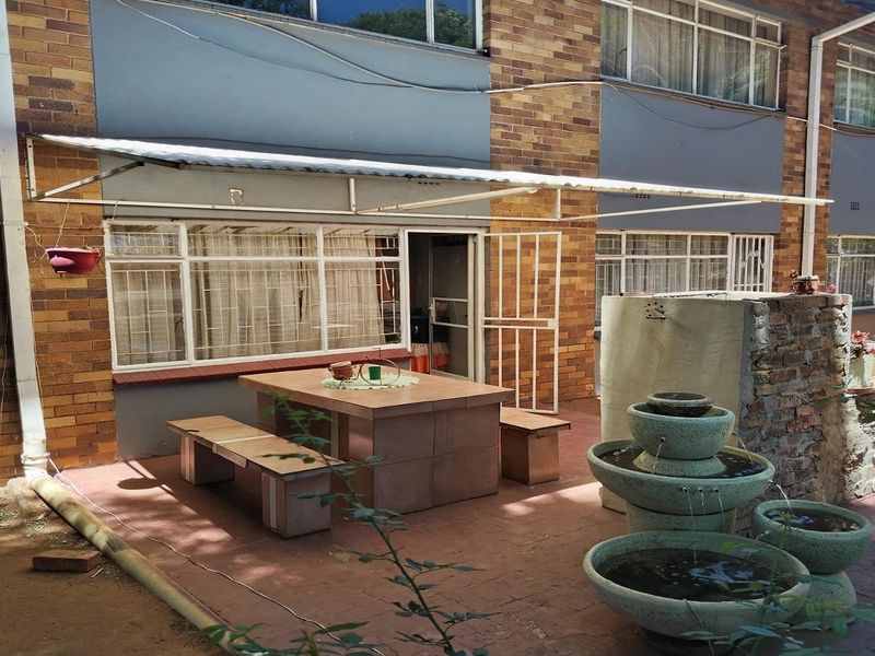 Rear exterior view of the apartment featuring a paved patio area, metal awning, and a stone water feature against a brick facade.