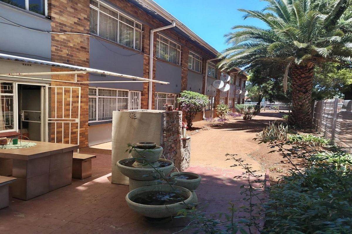 Rear exterior view of the apartment complex featuring a paved patio area, brick facade, and established garden surroundings.