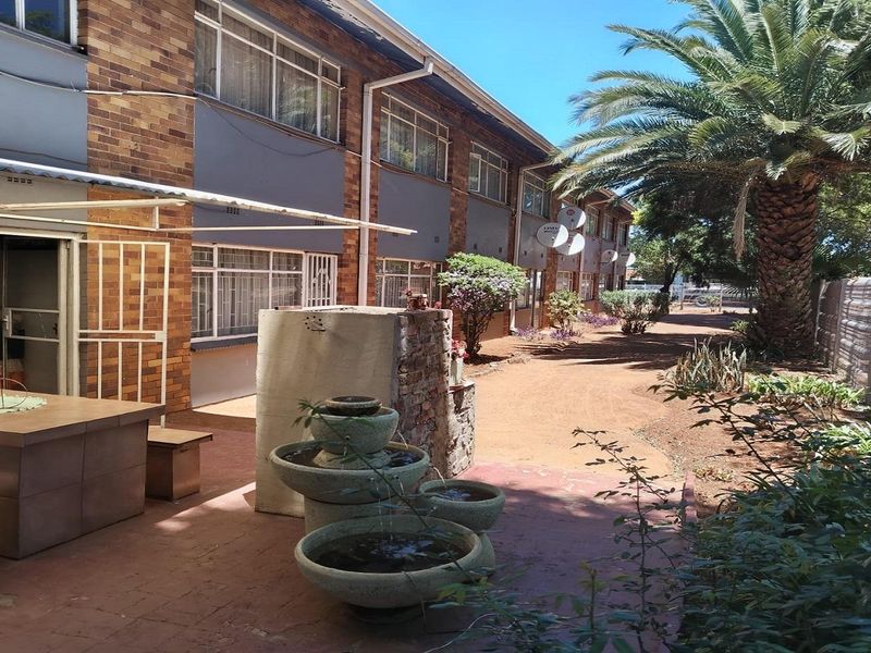 Rear exterior view of the apartment complex featuring a paved patio area, brick facade, and established garden surroundings.