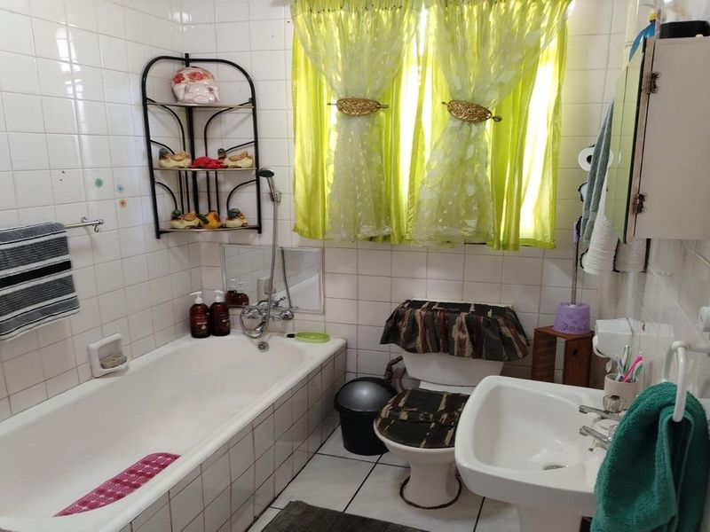 A functional bathroom featuring a bathtub, pedestal basin, and toilet, finished with classic white ceramic wall and floor tiles.