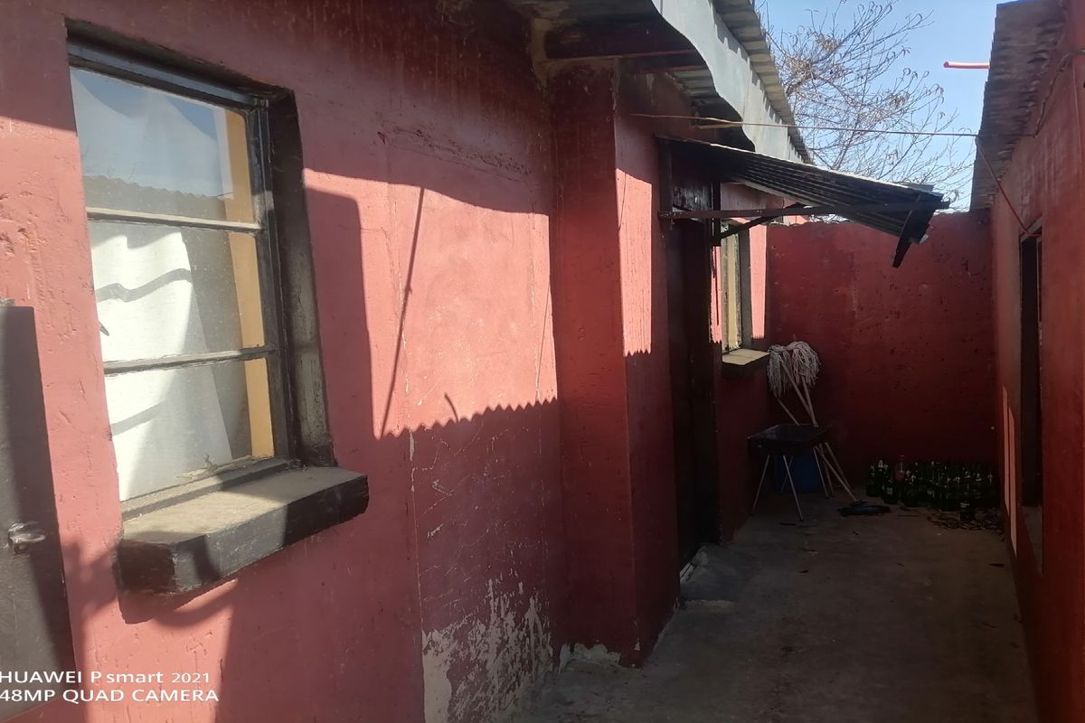 Rear exterior view of the property showing masonry walls with peeling paint and corrugated metal roofing.