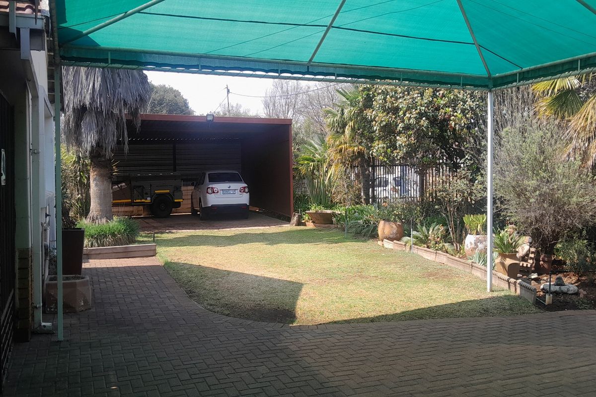 A spacious outdoor area featuring a paved driveway, a covered carport, and a landscaped garden with established trees and shrubs.