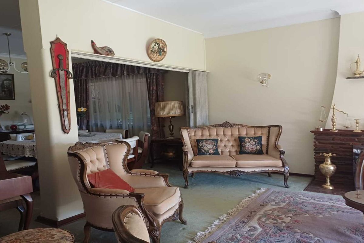 A traditional living room featuring a brick fireplace and an adjacent dining area, showcasing classic architectural proportions and neutral wall tones.