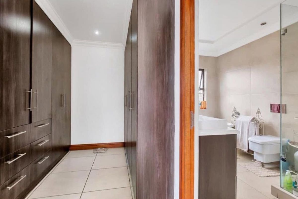 A well-appointed dressing area featuring extensive built-in dark wood cabinetry, leading directly into a modern en-suite bathroom with tiled finishes.