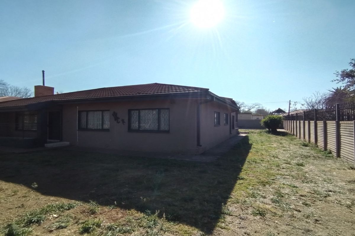 A view of the rear exterior of the house, featuring a tiled roof, brick perimeter wall, and a spacious backyard area.