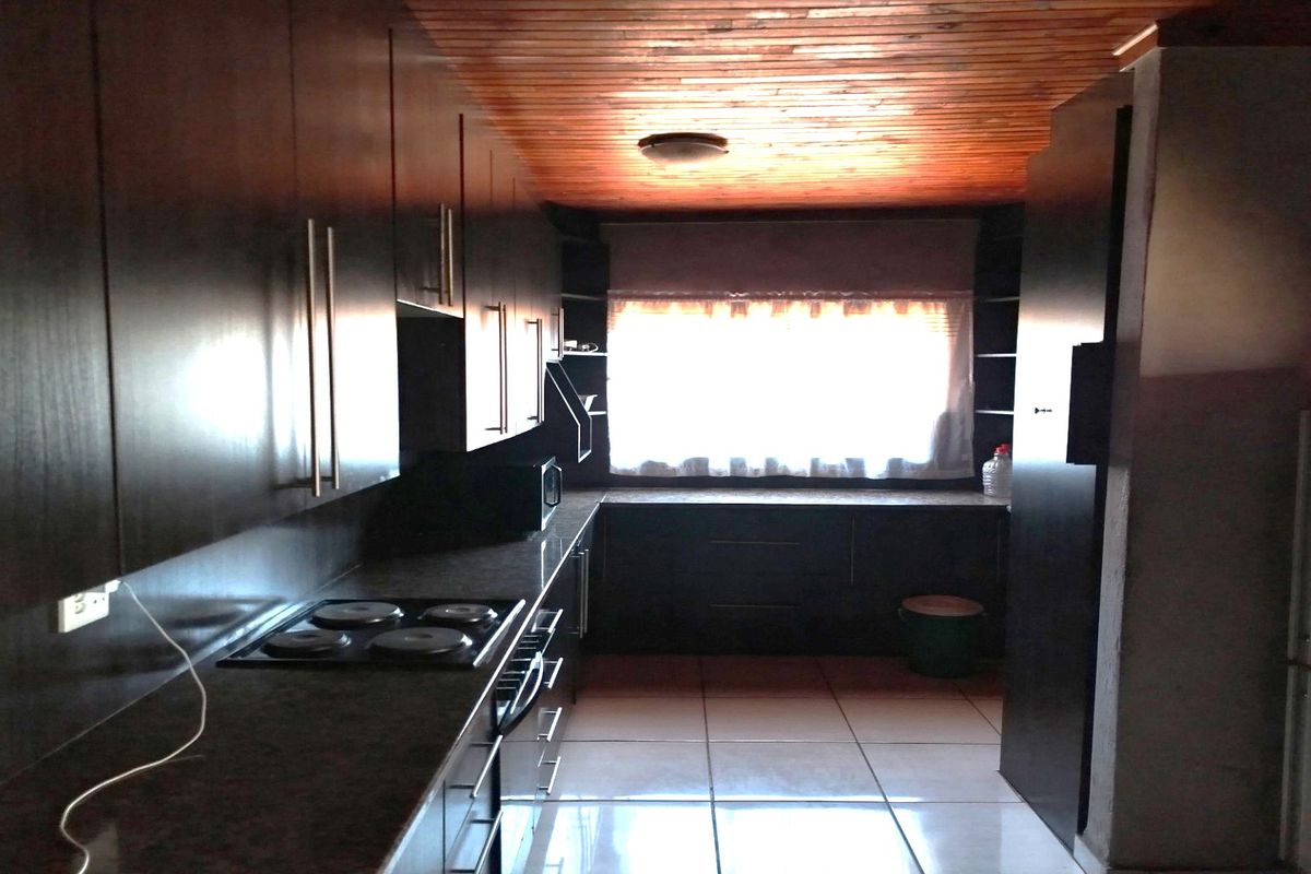 A galley-style kitchen featuring dark cabinetry, integrated electric hob, and tiled flooring under a timber-clad ceiling.