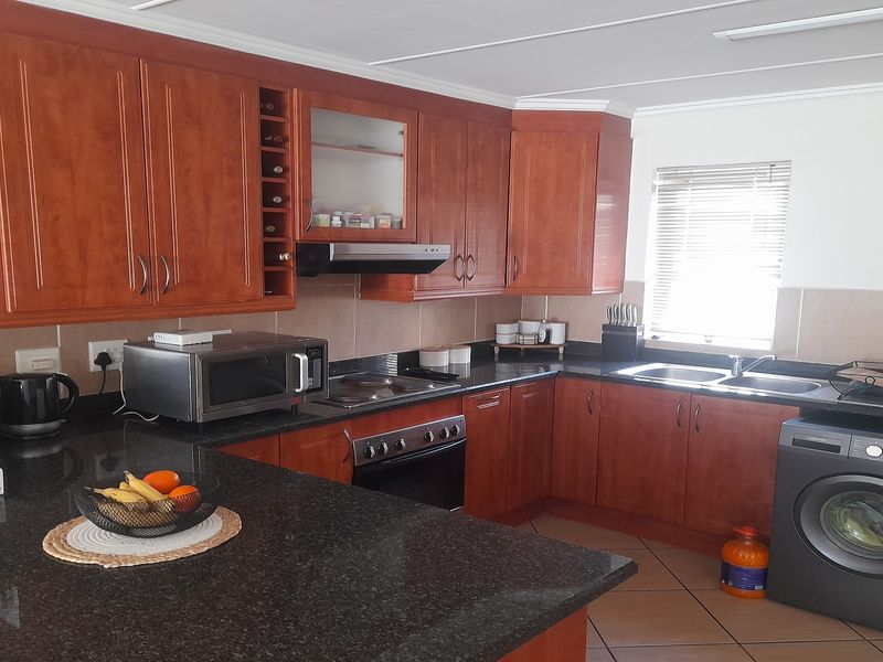 A functional kitchen featuring dark granite countertops, warm-toned wooden cabinetry, built-in oven, extractor fan, and a double sink with tiled flooring.