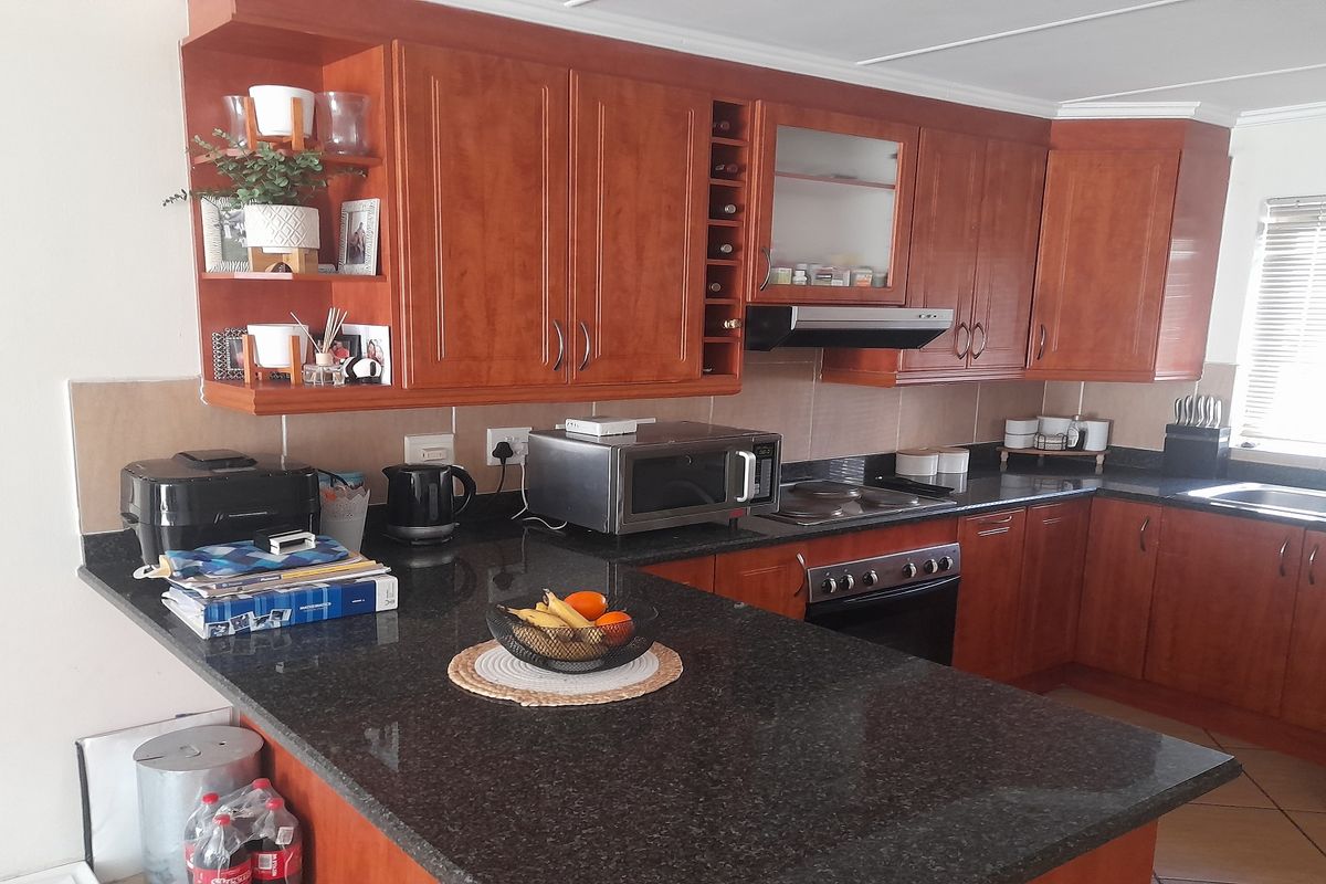 A functional kitchen featuring warm-toned wooden cabinetry, dark granite countertops, integrated appliances, and tiled flooring with ample workspace.