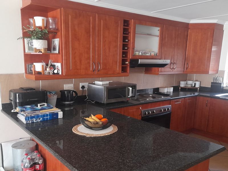 A functional kitchen featuring warm-toned wooden cabinetry, dark granite countertops, integrated appliances, and tiled flooring with ample workspace.