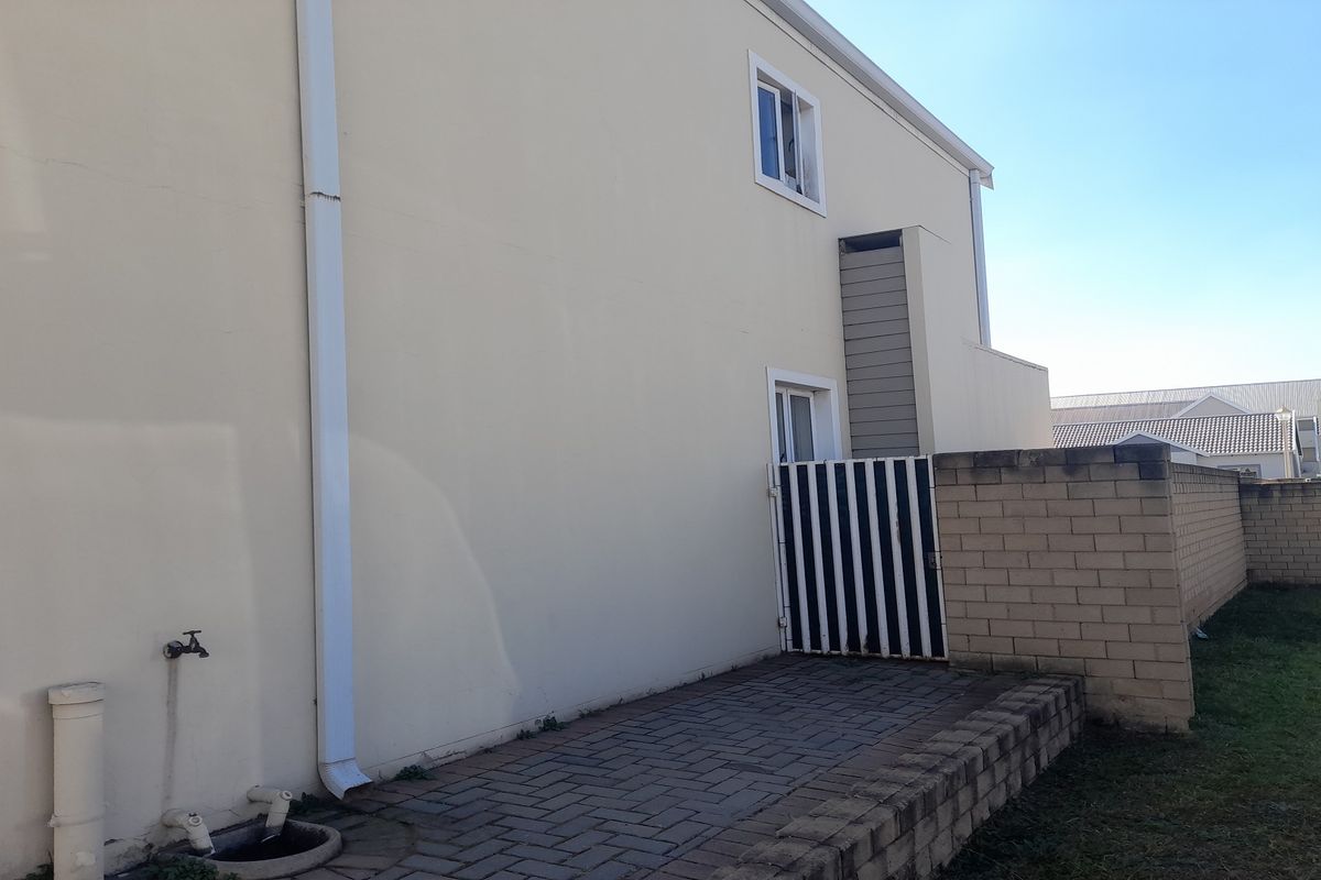 A view of the rear exterior of the property featuring a paved patio area, brick boundary wall, and external plumbing fixtures.