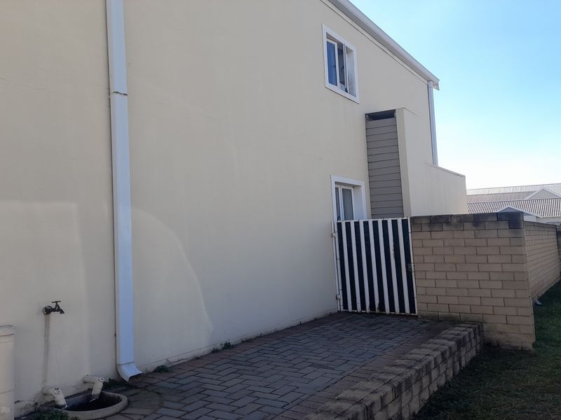 A view of the rear exterior of the property featuring a paved patio area, brick boundary wall, and external plumbing fixtures.