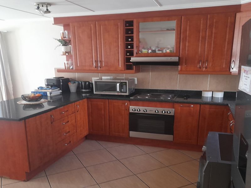A functional kitchen featuring warm-toned wooden cabinetry, granite countertops, a built-in oven with hob, and tiled flooring.