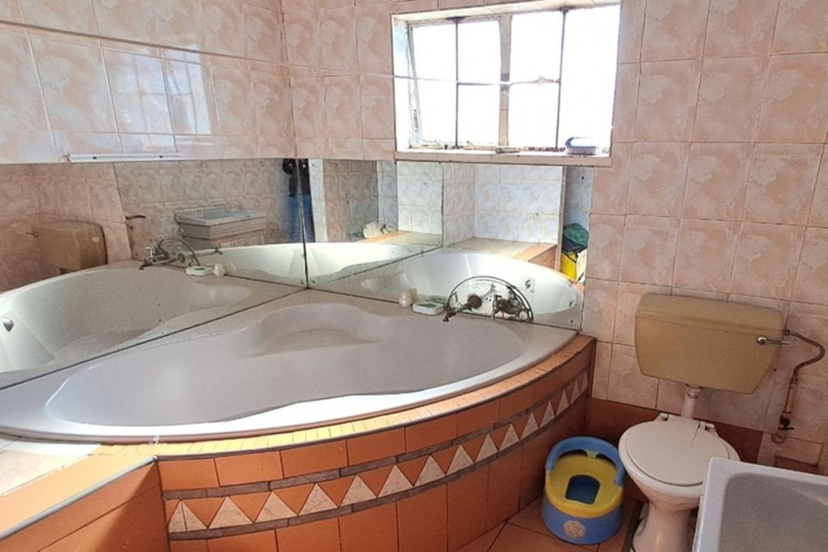 A dated bathroom featuring a corner bathtub, wall-to-wall mirror, and ceramic tiling throughout, requiring modernization to improve functionality and aesthetic appeal.