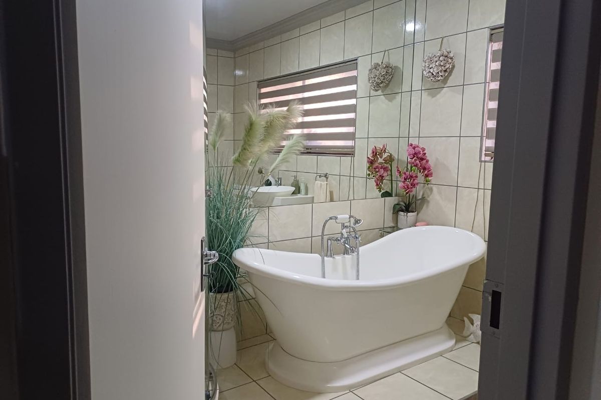 A well-maintained bathroom featuring a classic freestanding bathtub, tiled walls and flooring, and a large wall-mounted mirror.