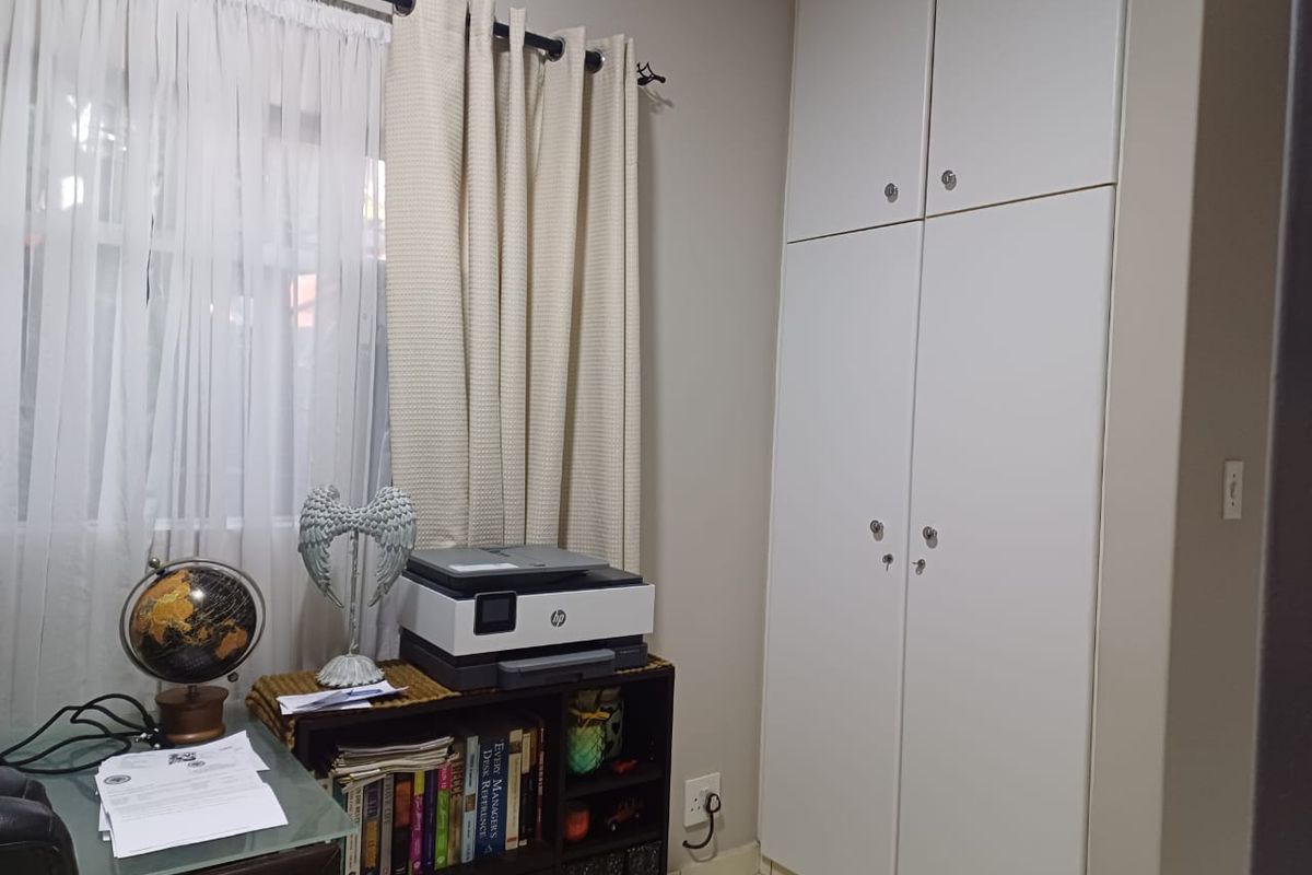 A functional bedroom featuring built-in floor-to-ceiling white cabinetry and a window with curtain treatments.