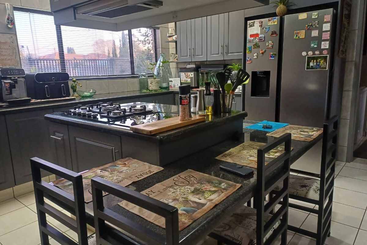 A modern kitchen featuring dark grey cabinetry, a central island with a built-in gas hob, granite countertops, and tiled flooring.