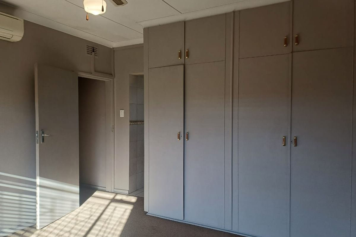 A bedroom featuring built-in cupboards, a ceiling fan, and an integrated air conditioning unit, with neutral wall tones and carpeted flooring.