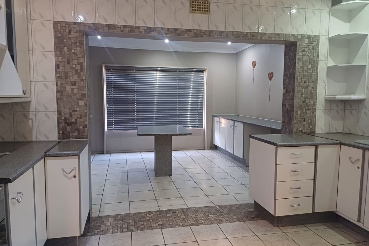 A spacious kitchen featuring tiled flooring, built-in cabinetry, and a central island, offering a functional layout with integrated storage and preparation areas.