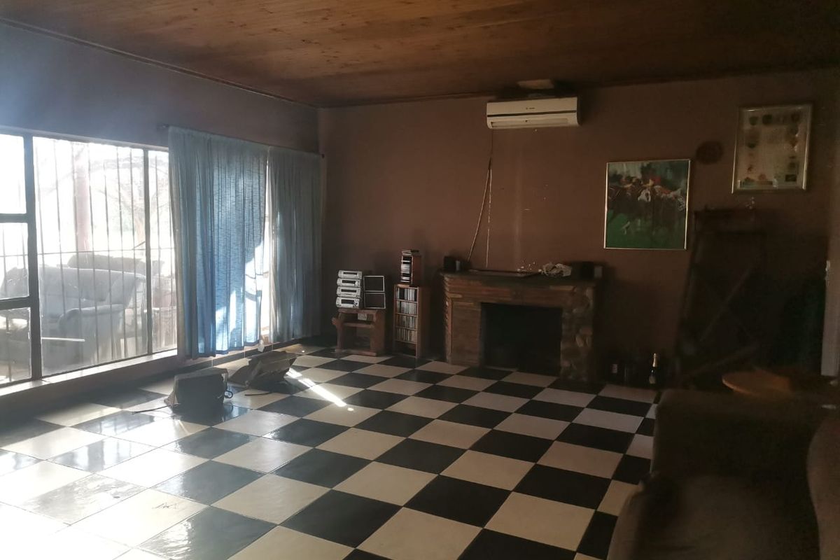 A living room featuring a checkerboard tiled floor, a stone-clad fireplace, and a timber-paneled ceiling, with large windows providing natural light.