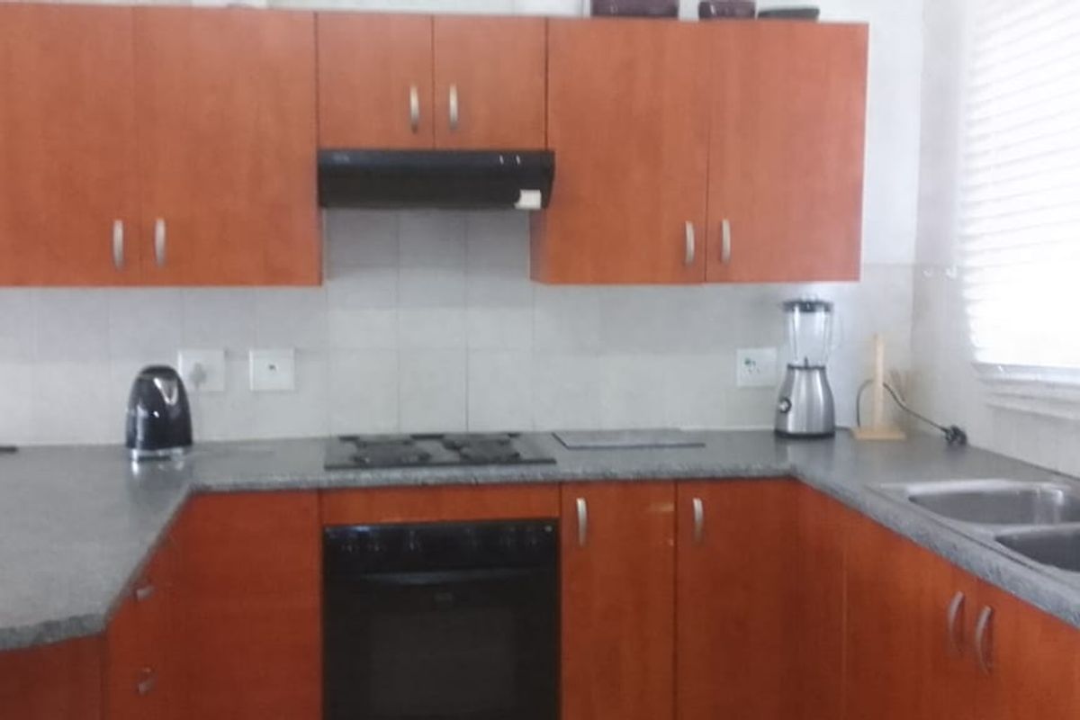 A functional kitchen featuring wood-finish cabinetry, a built-in oven, a hob with an extractor fan, and a double-basin sink with a tiled backsplash.