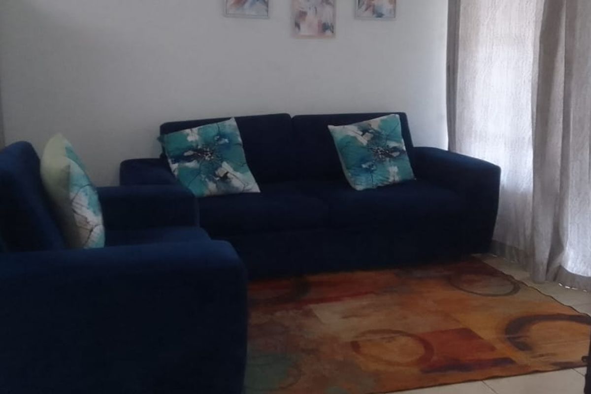 A living room area featuring tiled flooring and large windows with curtains, providing a functional space for relaxation.