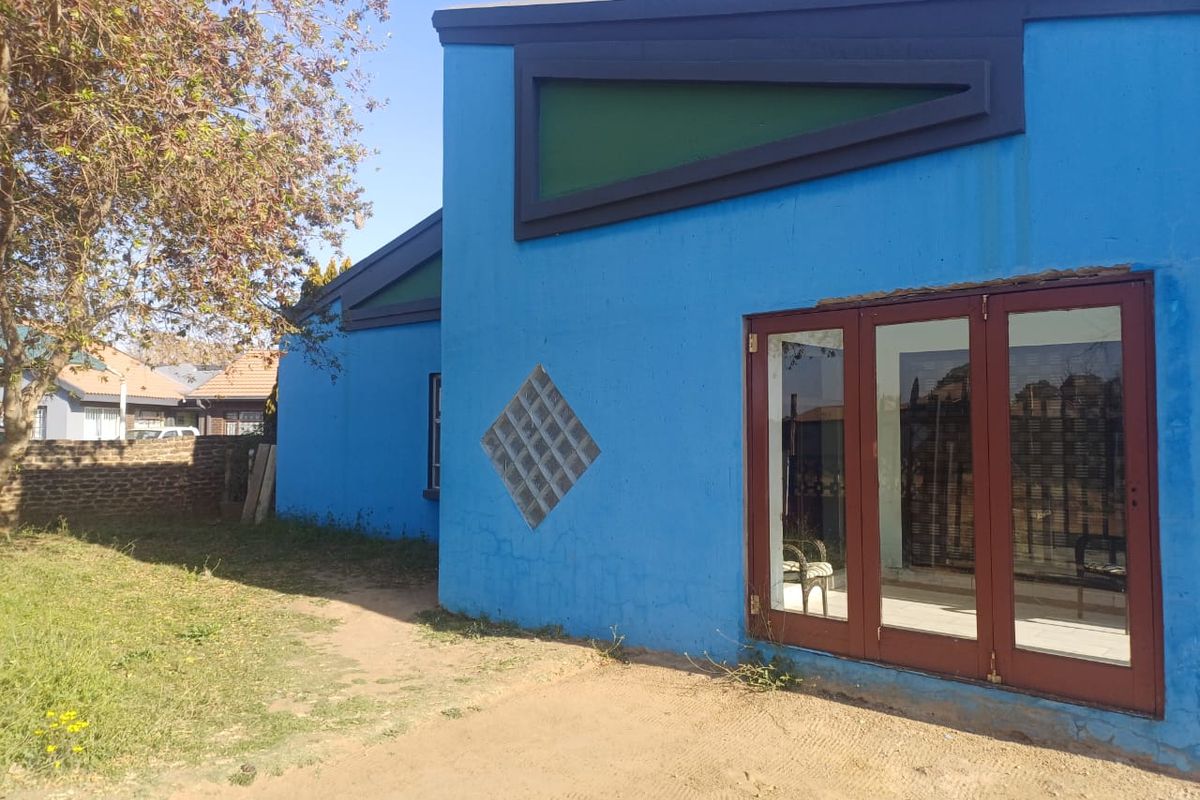 Exterior view of the rear facade featuring blue painted walls, triangular accent windows, glass block detailing, and brown framed glass doors.