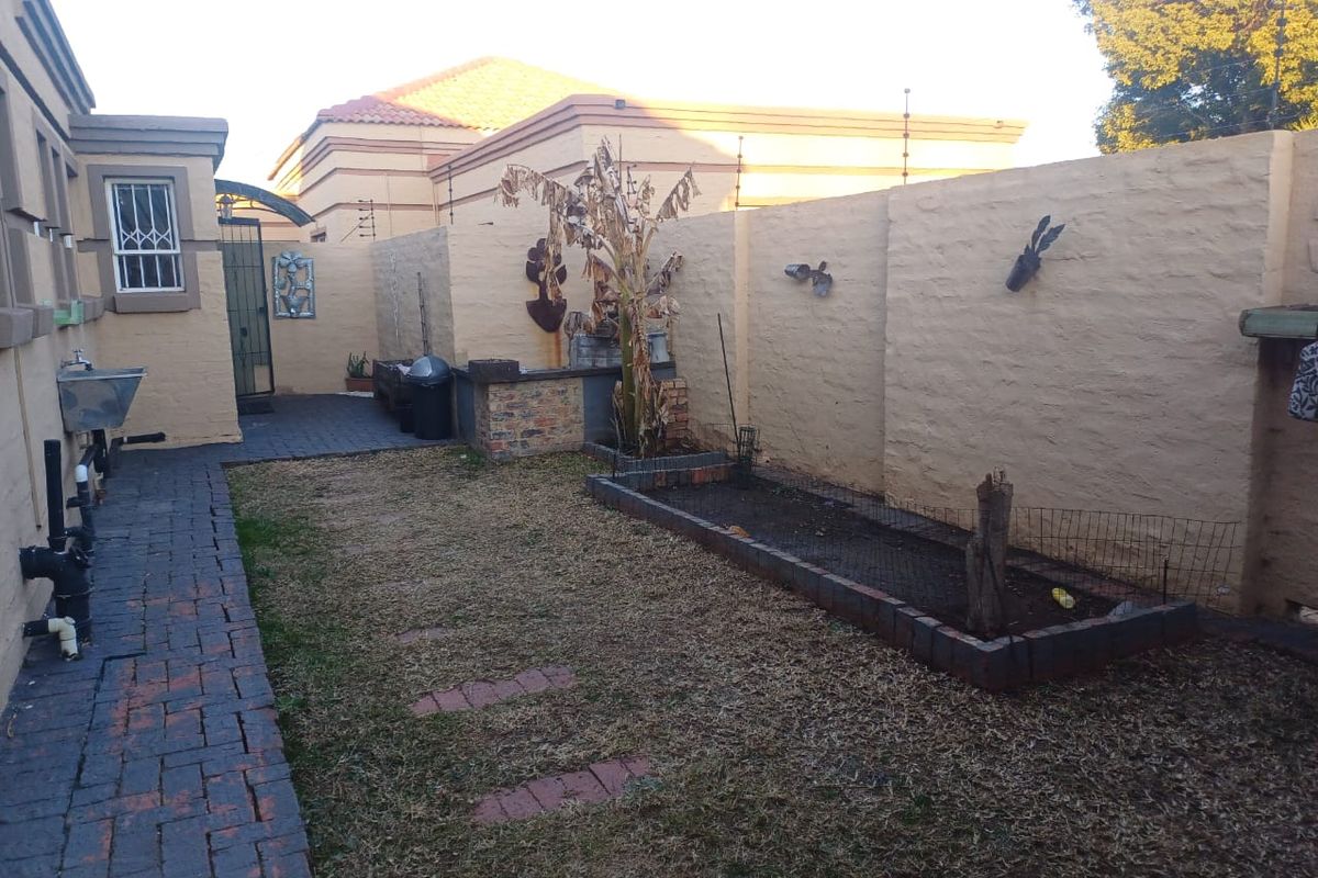 A private rear courtyard featuring paved walkways, a built-in brick planter, and perimeter boundary walls with security fencing.