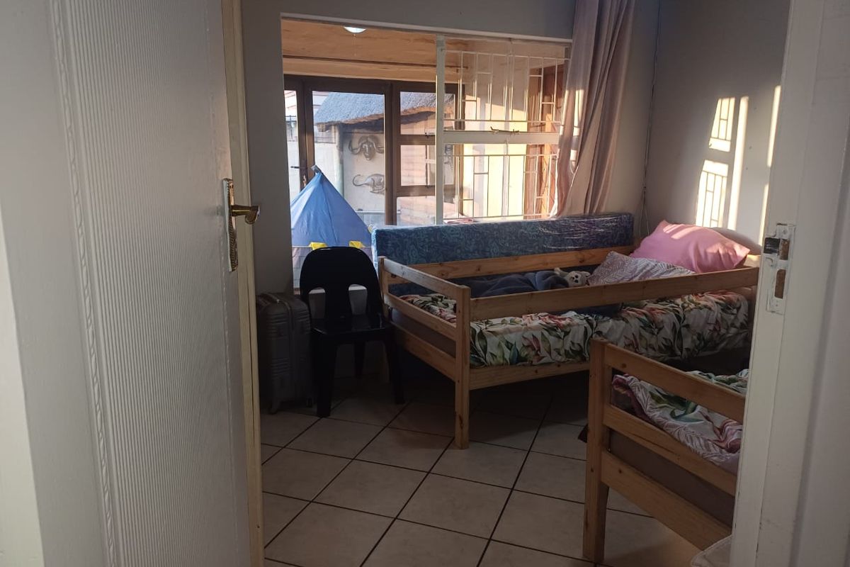 A bedroom featuring tiled flooring and a large window with security bars, providing natural light and a view of the outdoor area.