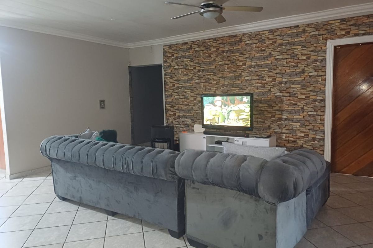 Spacious living room featuring a decorative stone-cladding feature wall, tiled flooring, and a ceiling fan.