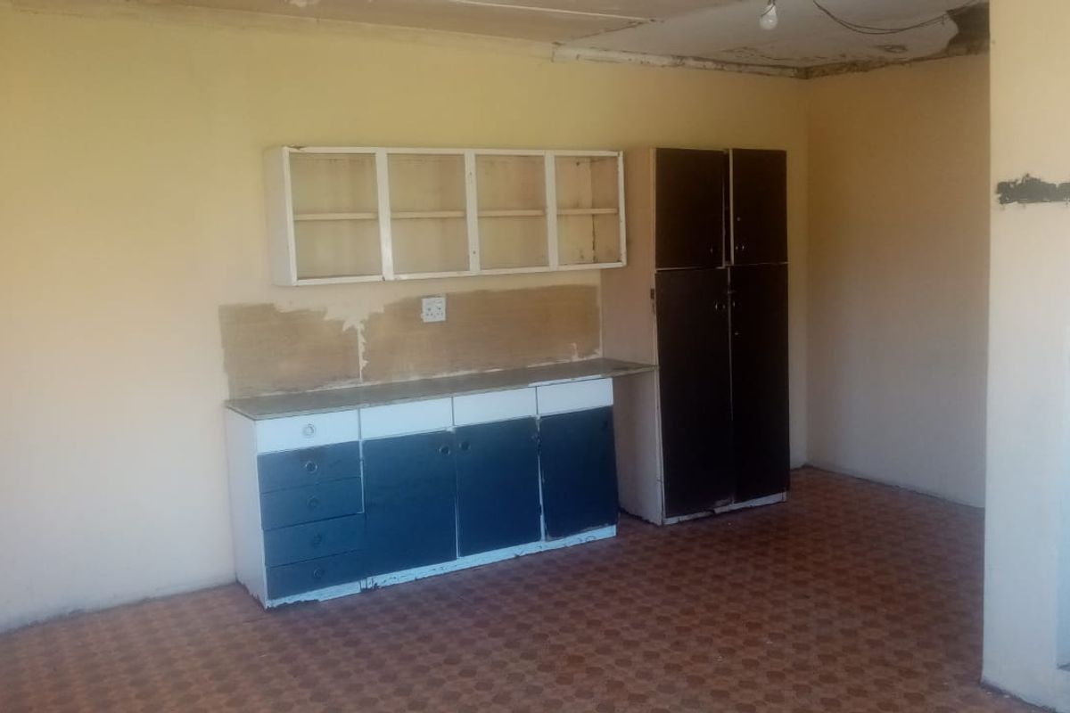 A dated kitchen area featuring basic built-in cabinetry, a tall storage unit, and original flooring, requiring significant renovation and cosmetic updates.