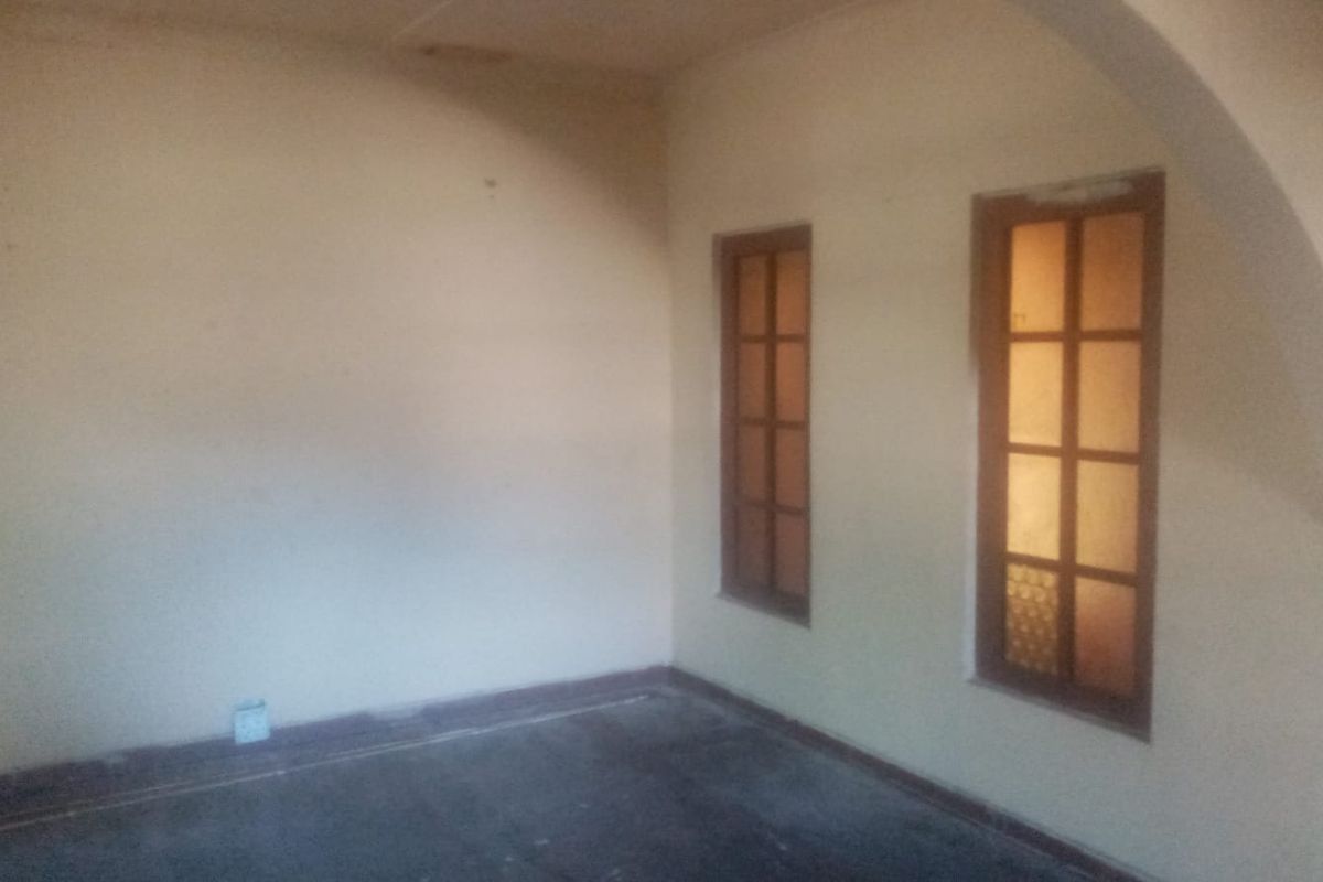 An empty interior room featuring two wooden-framed windows and an arched wall detail, offering a blank canvas for renovation.