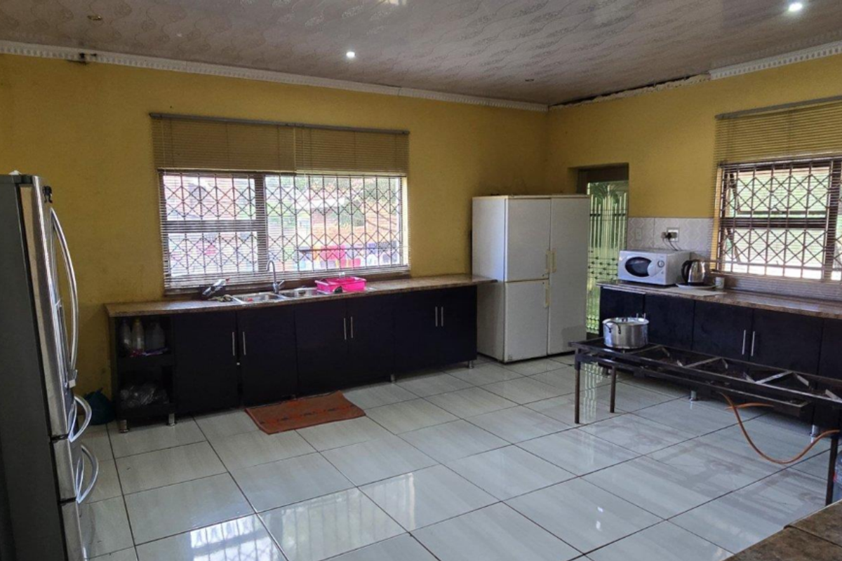 Spacious kitchen featuring dark cabinetry, tiled flooring, and large windows with security bars, offering ample counter space and functional layout.