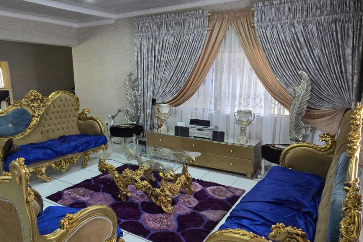 A spacious living room featuring tiled flooring, decorative ceiling molding, and a tiled pillar, providing a formal area for relaxation and entertainment.