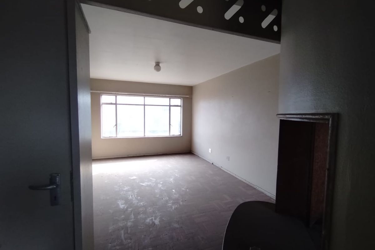 An empty living room featuring parquet flooring, large windows providing natural light, and a decorative archway leading into the space.