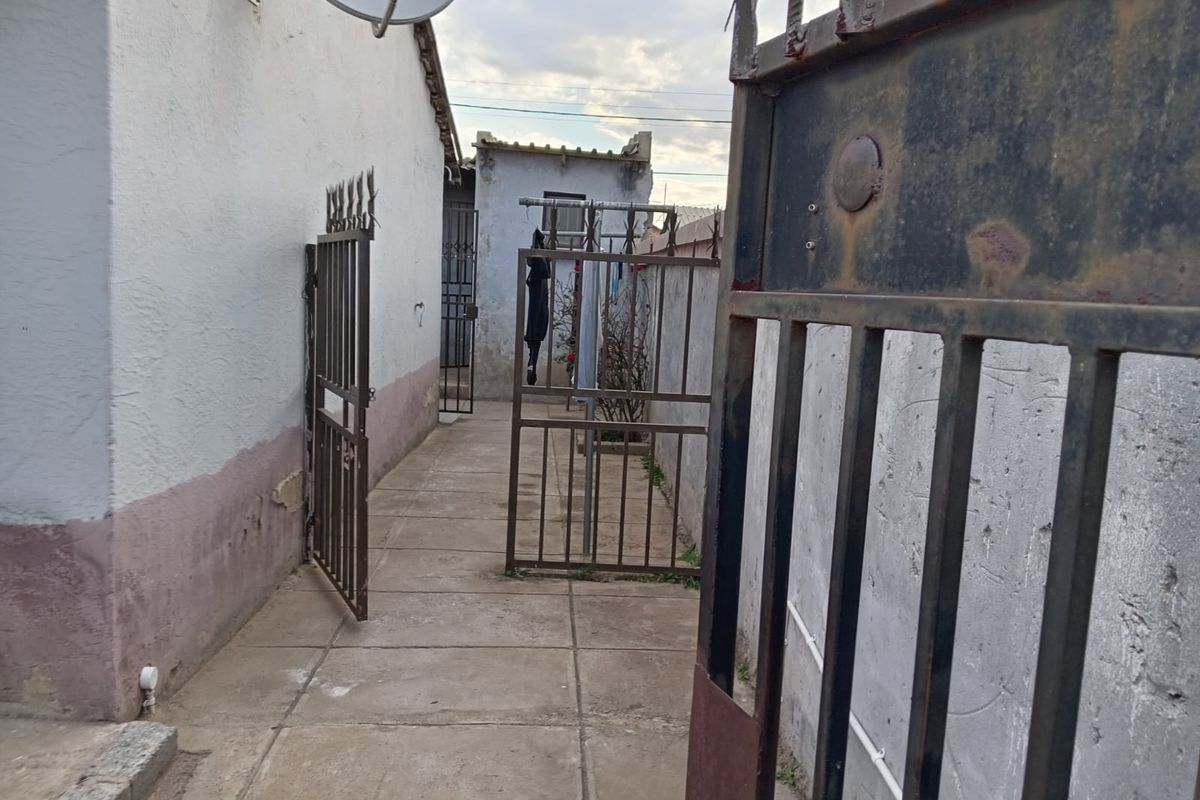 A narrow side passage featuring concrete paving, metal security gates, and exterior wall access.