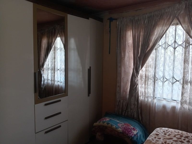 A bedroom featuring built-in cabinetry with a mirrored panel and a window fitted with security bars.