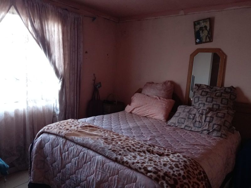 A bedroom featuring a window with curtains and a built-in mirror, showing signs of wear on the wall surfaces.