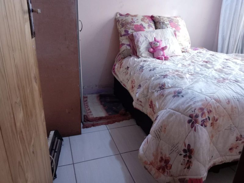 A compact bedroom featuring tiled flooring and a built-in wooden cupboard, showing signs of wear and tear.